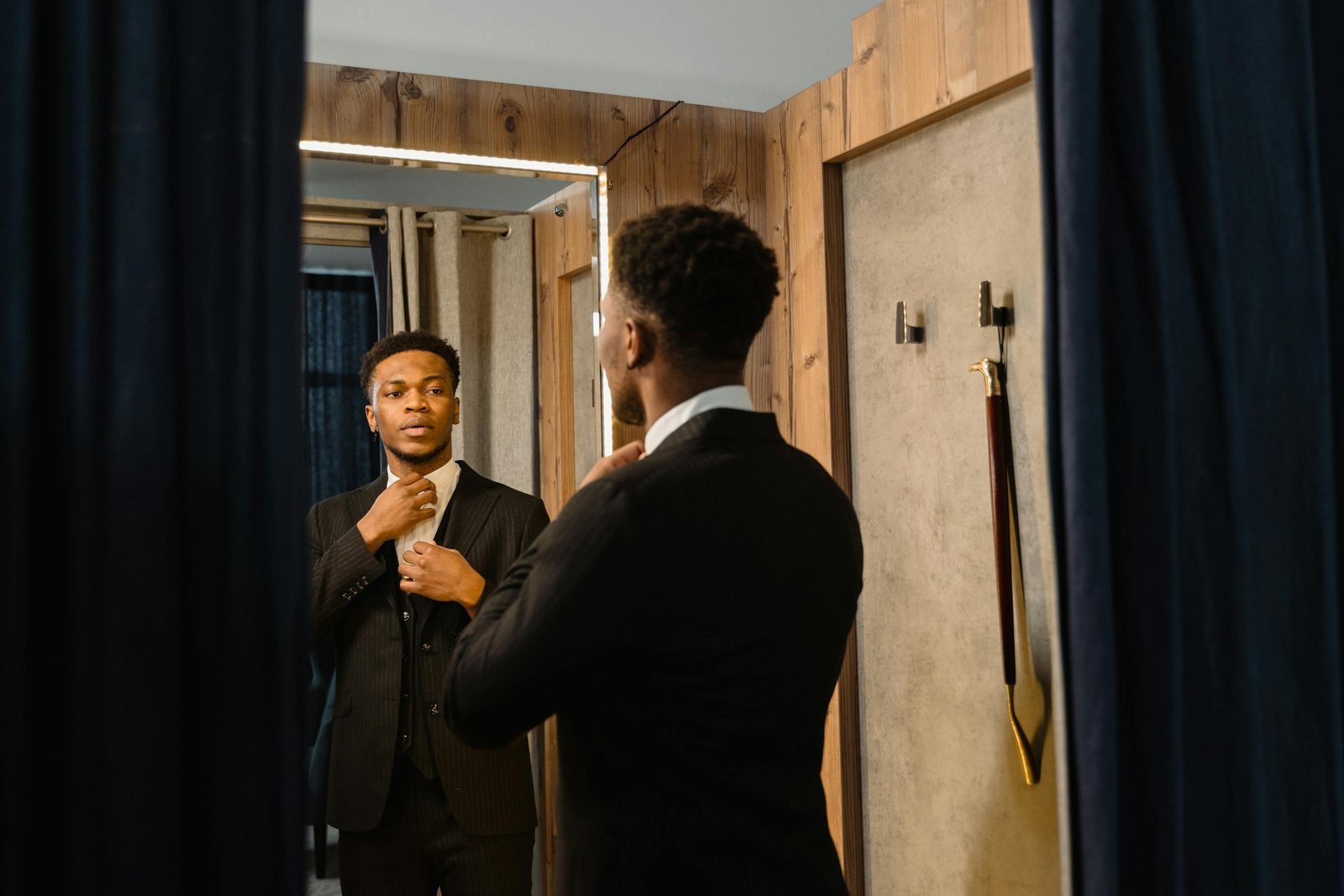 Stylish man adjusts his tie in a fitting room mirror, reflecting business confidence.